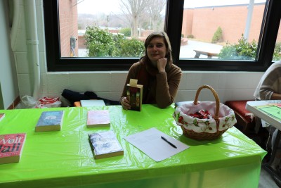 Student poses with book at club day table