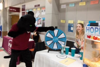 PVCC mascot Pounce the panther spins a wheel for a prize at the Hope club table while Madison Weikle laughs.