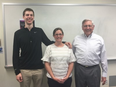 Three people stand in front of a whiteboard in a classroom. 