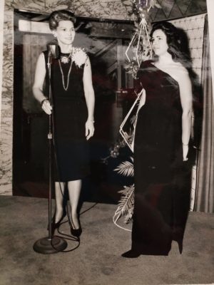 Addie Smith (right) stands in room next to another woman. Both women are wearing dresses. 