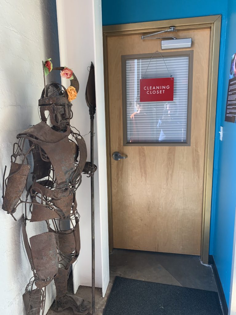 Entrance to the exhibit. A person made of rusted metal wielding a spear greats visitors. It has several colorful flowers adorning its head.