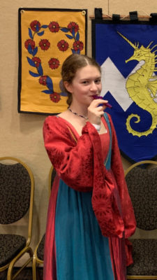 Zmick in a medieval-style red dress. She is also holding a purple kazoo.