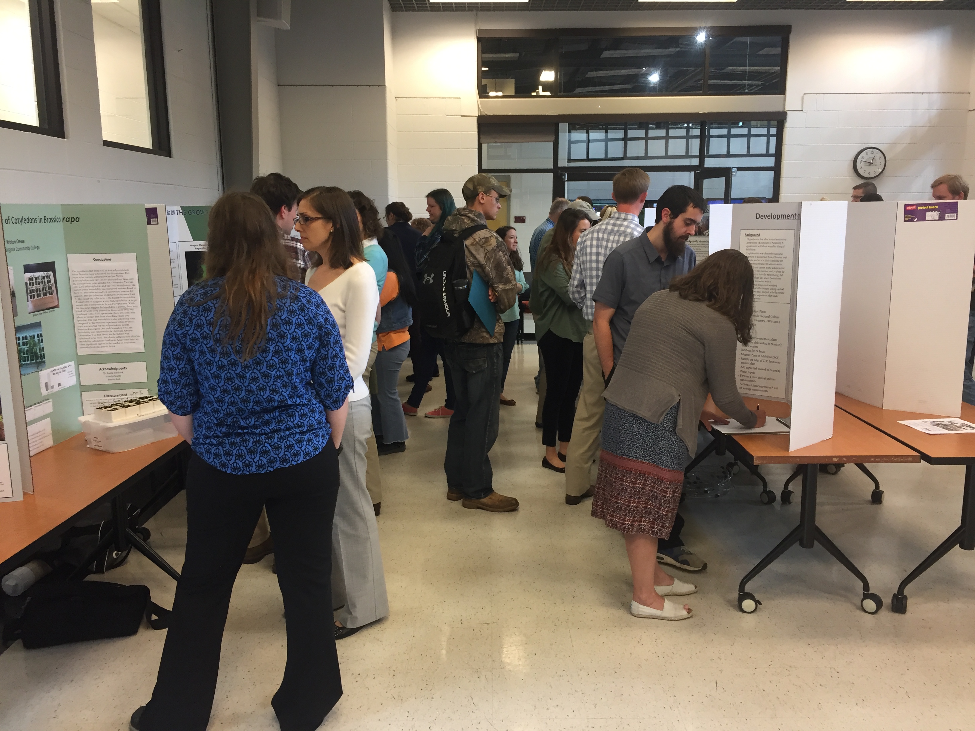 Students and faculty look at posters on tables in the North Mall Meeting Room.