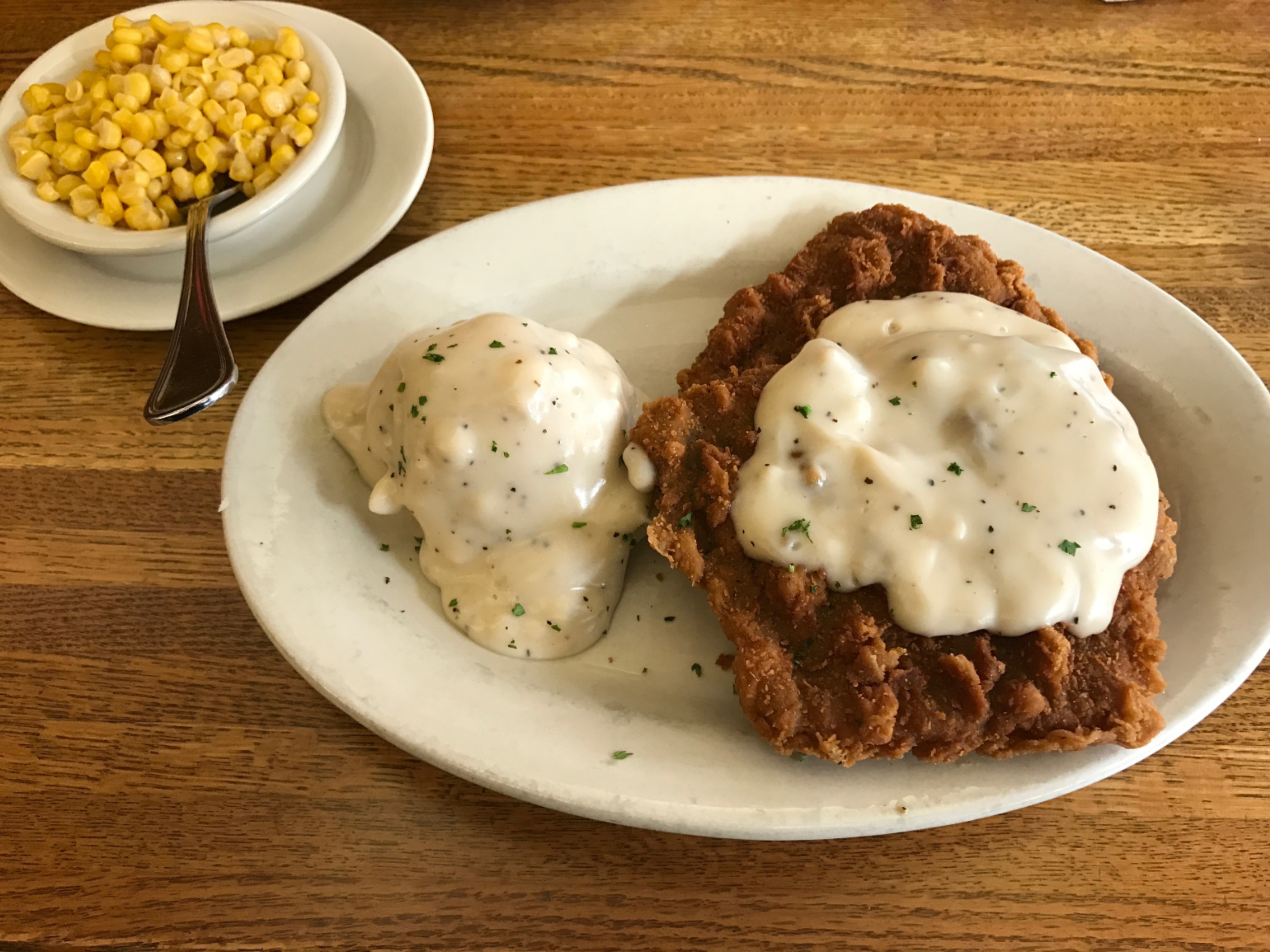 a picture of meat , potatoes and corn where the meat and corn have a white gravy on top