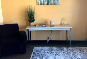 Photograph of the Retreat Room. A table with plants sits on a white rug next to a brown chair.