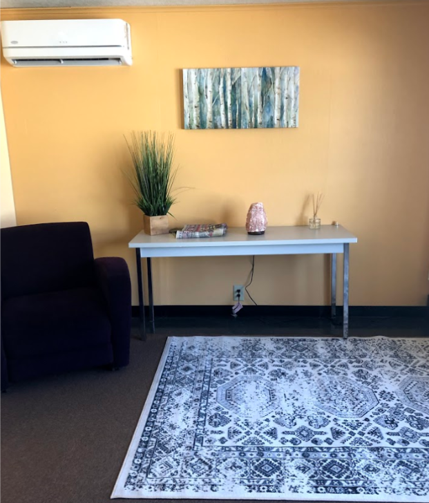 Photograph of the Retreat Room. A table with plants sits on a white rug next to a brown chair.