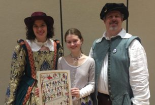 Zmick, standing in medieval attire with two other members of her reenactment group. Zmick is holding an award decorated with drawings of medieval dancers.