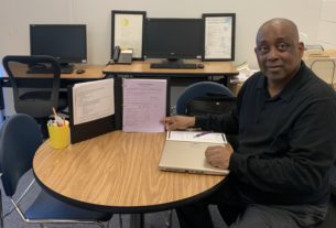 James Bryant, an academic coach, sits at a table. He is pointing at an open three-ring binder with an academic coaching handout inside.