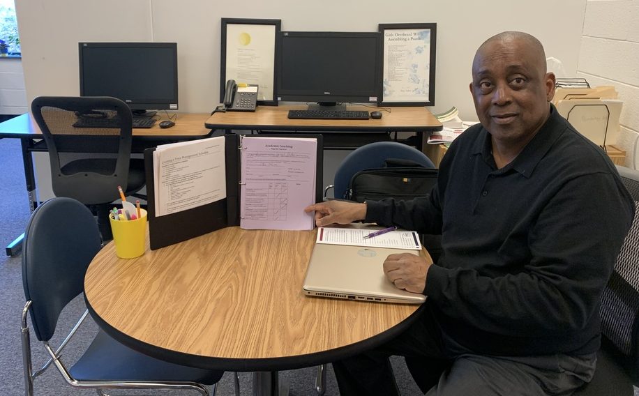 James Bryant, an academic coach, sits at a table. He is pointing at an open three-ring binder with an academic coaching handout inside.