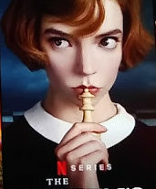a photo of the queen's gambit netflix poster, a young redheaded woman (anna taylor-joy) holds a chees piece to her lips and looks thoughtfully to the left.