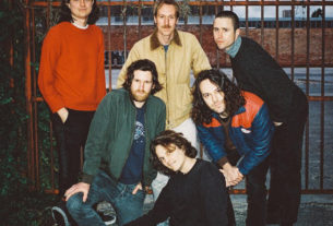 The members of King Gizzard stand in front of an iron gate