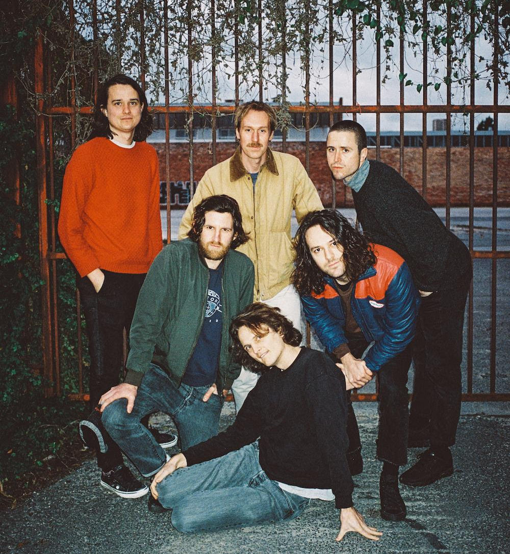 The members of King Gizzard stand in front of an iron gate