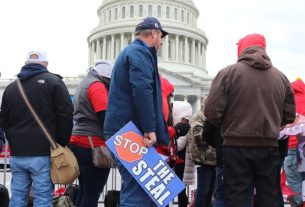 A man holding a "stop the steal" sign stands in a crowd in front of the Capitol Building