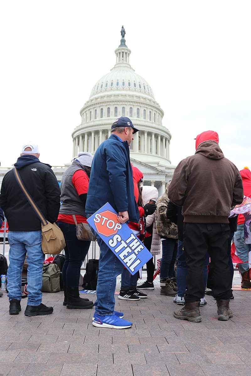 A man holding a "stop the steal" sign stands in a crowd in front of the Capitol Building