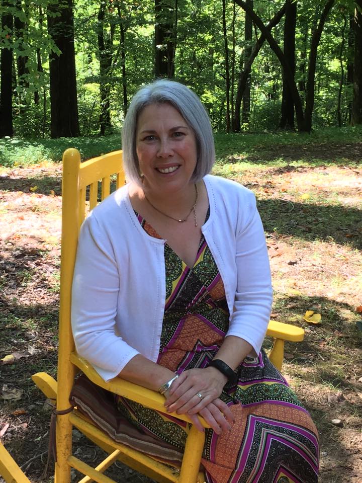 Rebecca Payton smiles at the camera while sitting in a yellow rocking chair on a sunny day