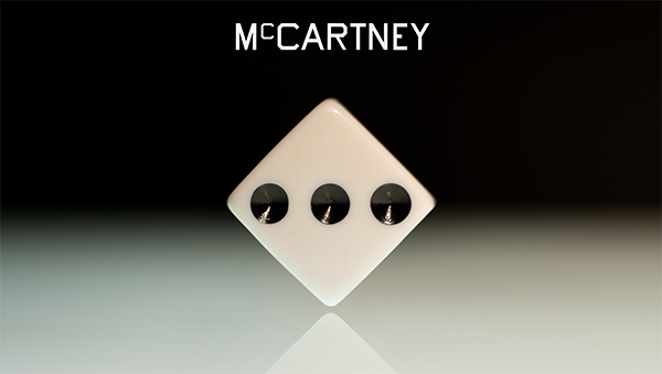 the name "McCartney" in white lettering hovers above a white dice with three black pips