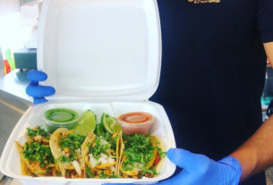 Four tacos in a white takeout container.