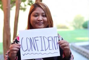 A woman holds a paper sign that reads "confident"