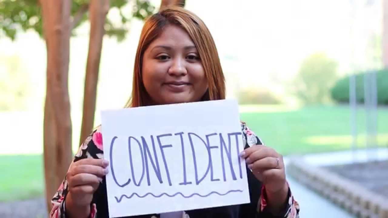 A woman holds a paper sign that reads "confident"