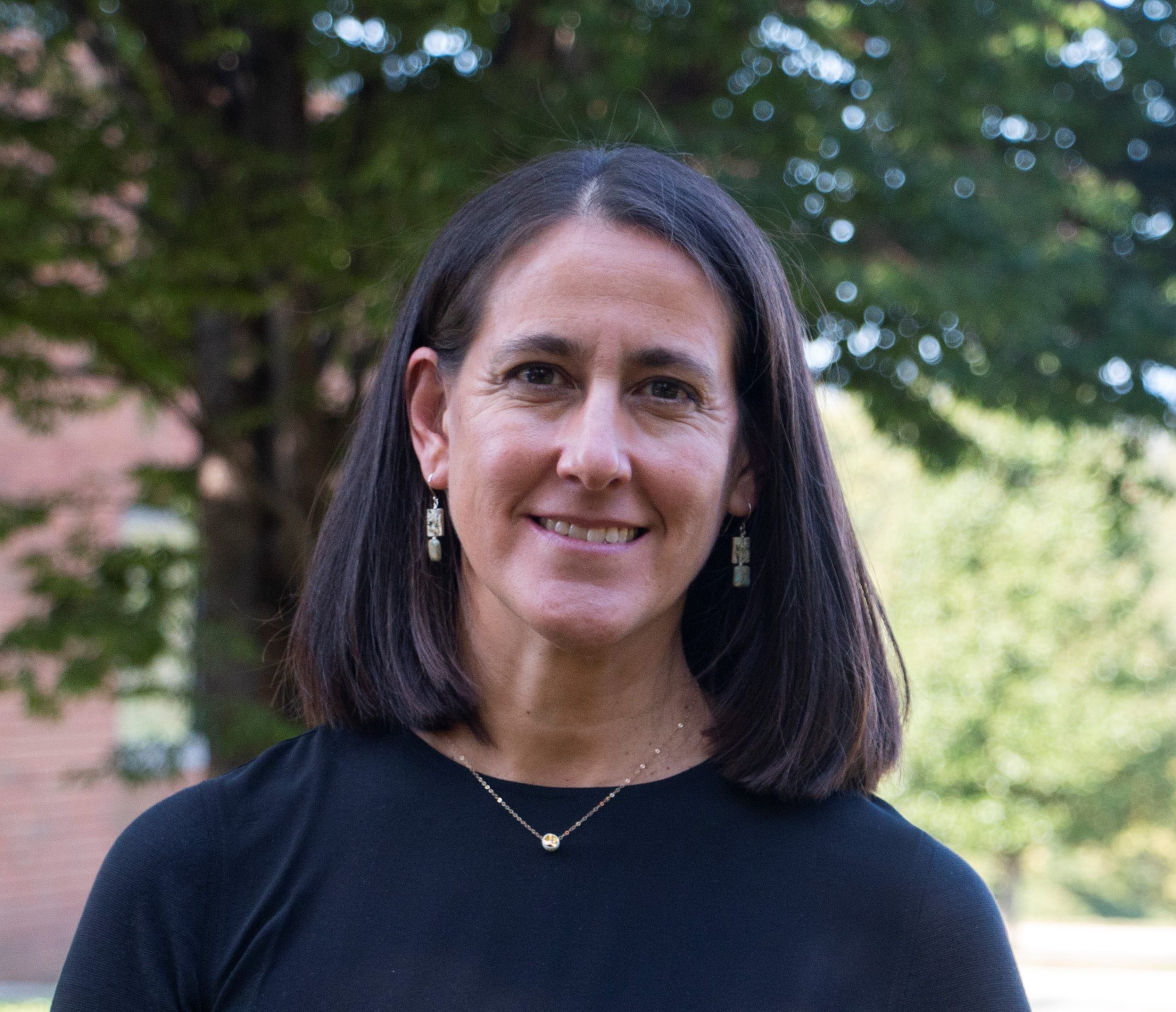 Jennifer Koster, a woman with shoulder length brown hair, smiles and tilts her head slightly.