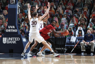 A basketball player in white (number 30) blocks a basketball player in red