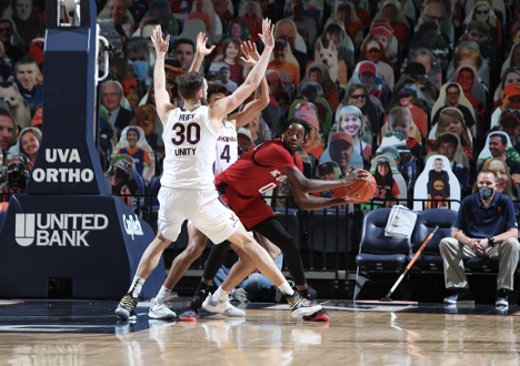 A basketball player in white (number 30) blocks a basketball player in red