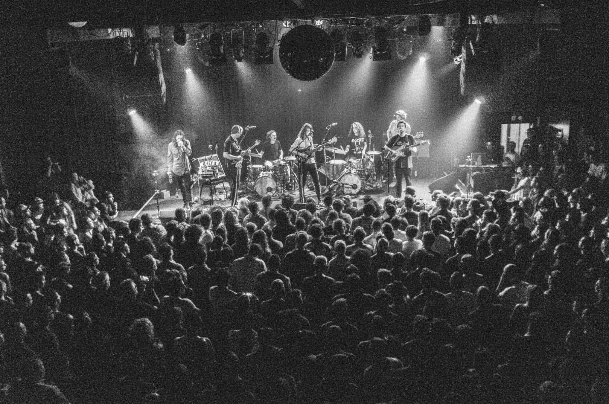 In a black and white photo, the members of King Gizzard perform live at a concert surrounded by a crowd of their fans