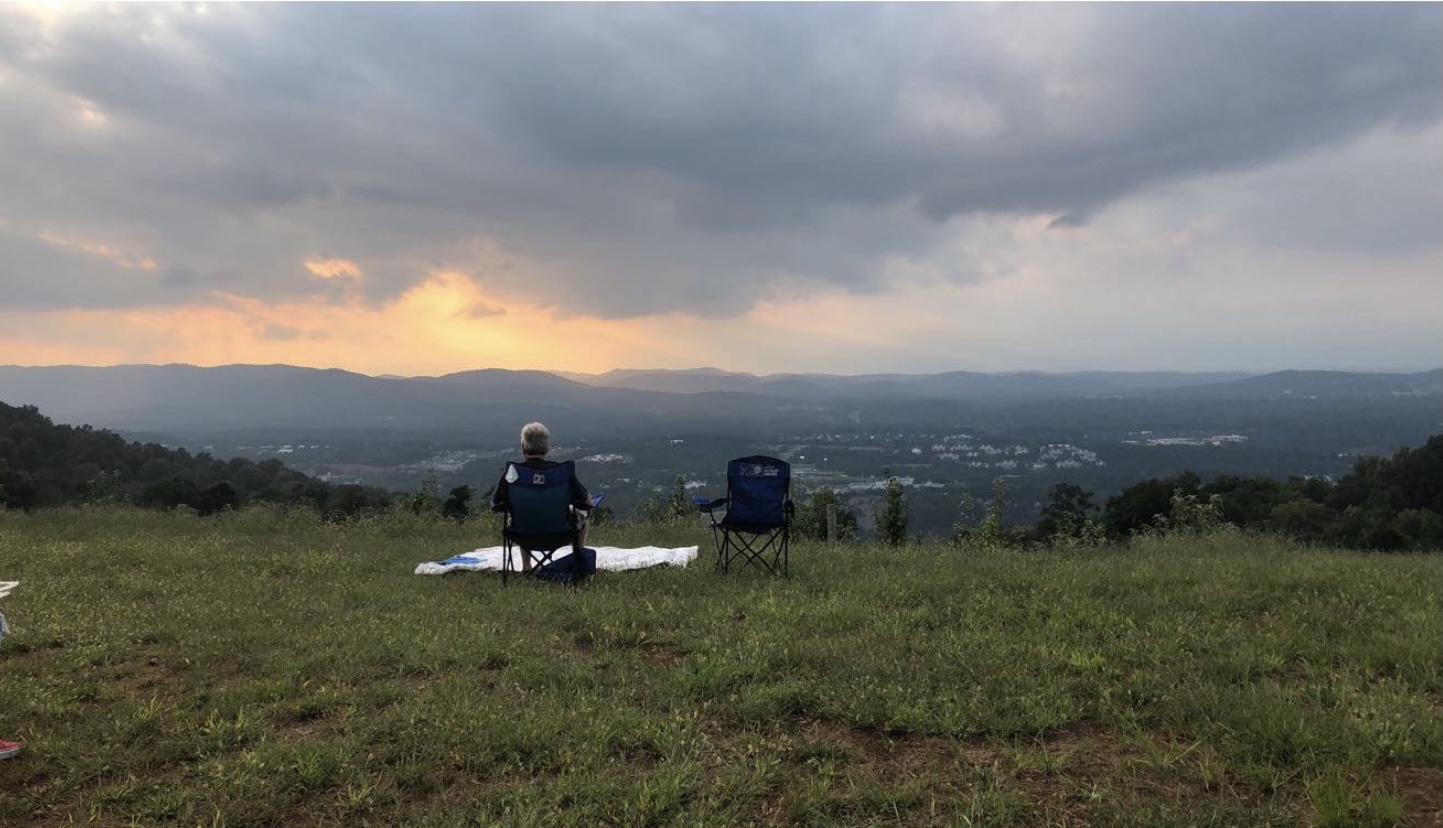 Man sits on the lawn of Carter Mountain, overlooking the city below and the sunset.