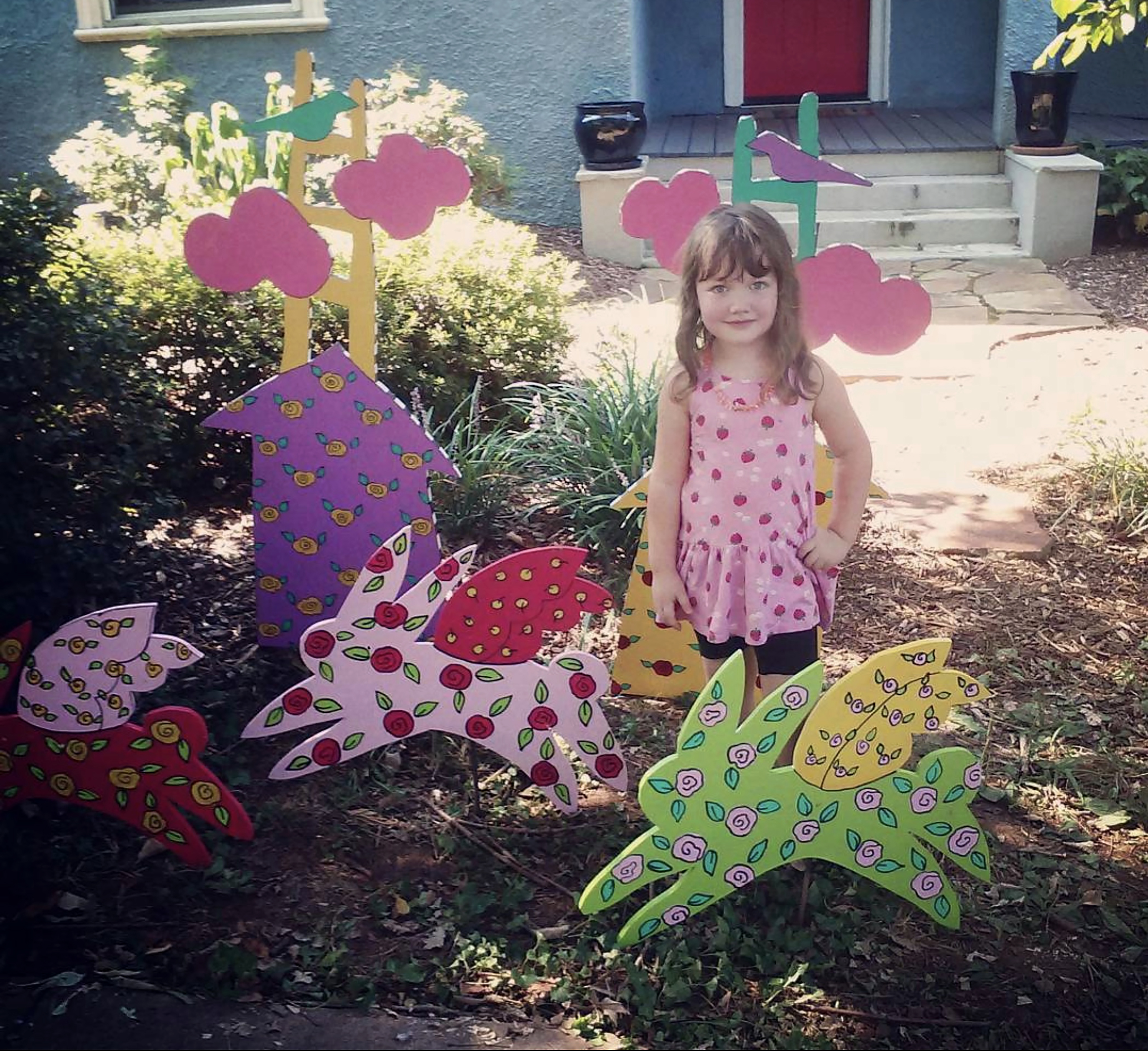 Margot, a young girl, stands among a collection of painted rabbit cut outs. Margot's dress matches the pattern painted on the rabbits.