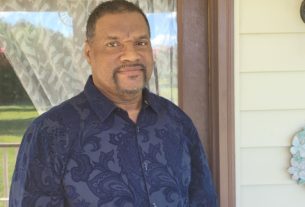 PVCC Professor Bruce Robinson stands on his porch in a blue shirt