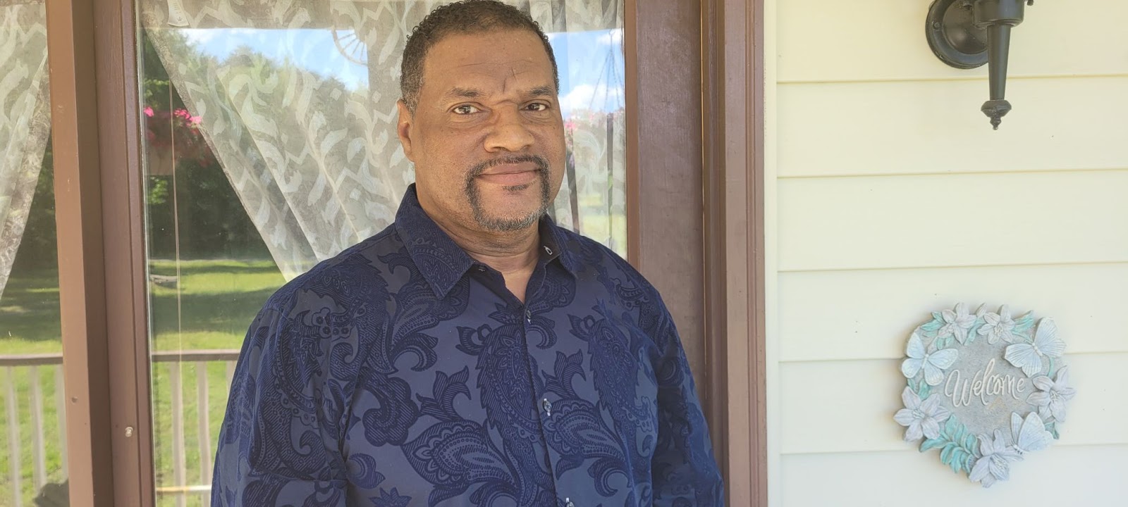 PVCC Professor Bruce Robinson stands on his porch in a blue shirt
