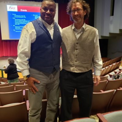 Bruce Robinson stands in a blue vest next to David Lerman in a gold vest in the PVCC auditorium 