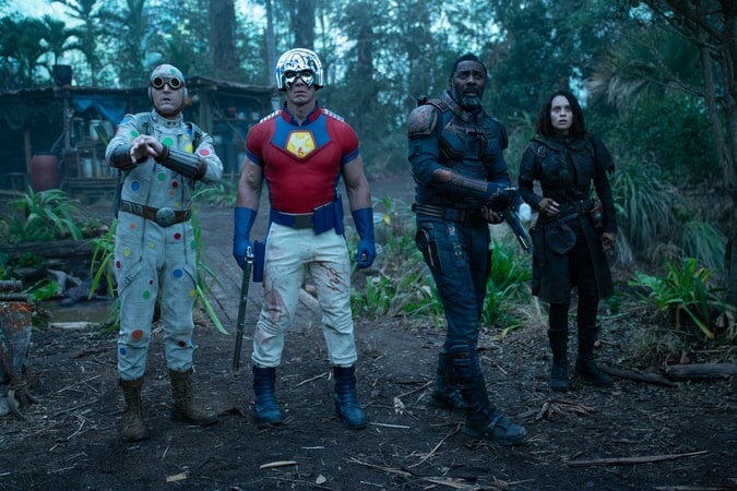 Four members of the suicide squad, three men in colorful costumes and a woman, stand in a jungle