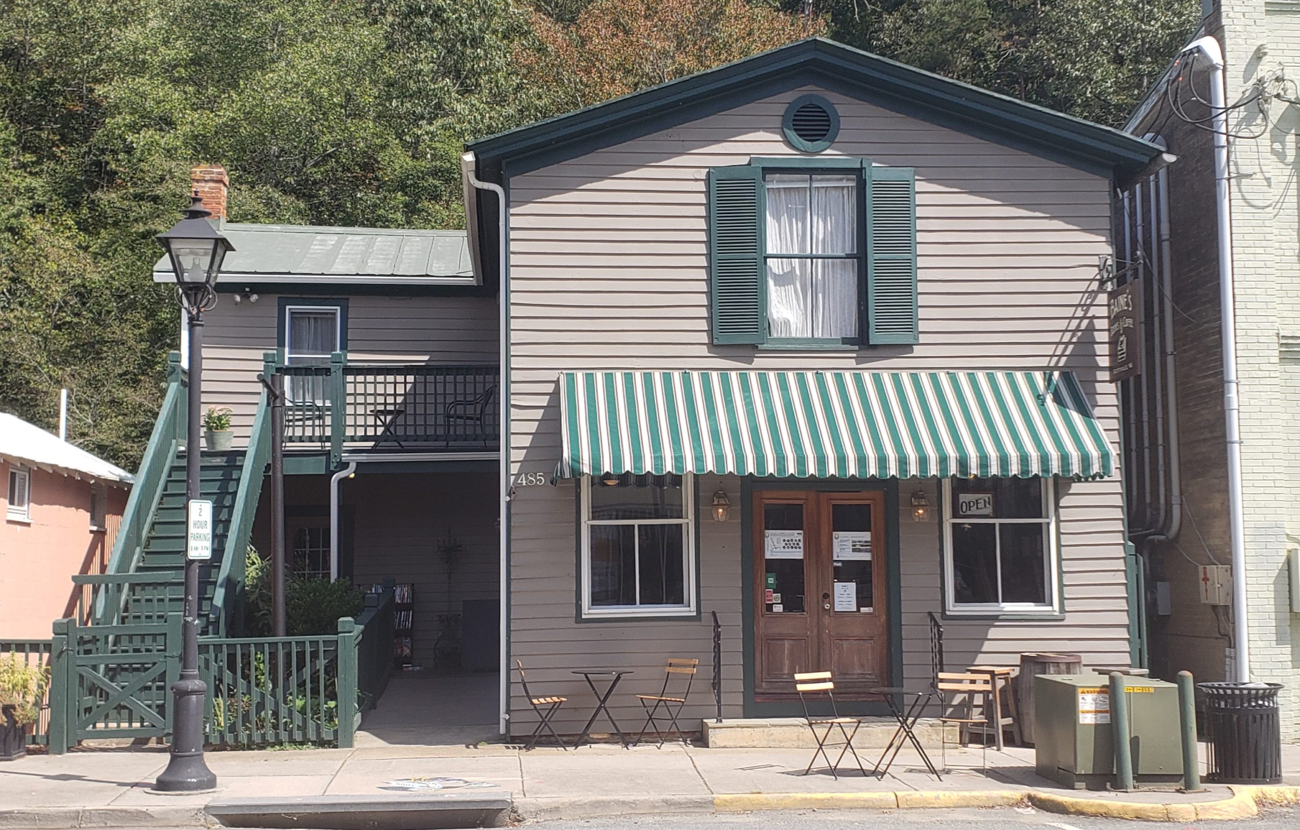 A quaint building with a green colored roof and a tan front with brown double doors