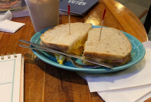 Two breakfast sandwiches sitting on a blue plate, with a chai latte in a plastic cup in the background