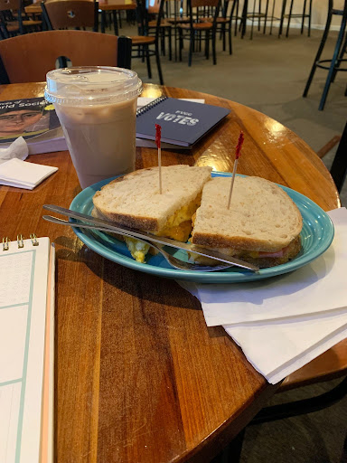 Two breakfast sandwiches sitting on a blue plate, with a chai latte in a plastic cup in the background