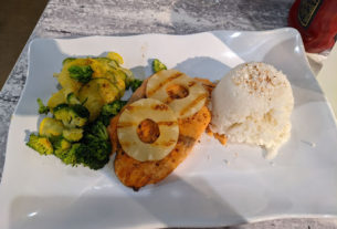 A plate of food with some ice cream, vegetables, and fried salmon topped with pineapple slices