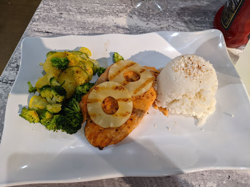 A plate of food with some ice cream, vegetables, and fried salmon topped with pineapple slices