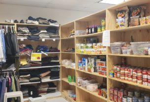 A wide shot of a food pantry stacked with cans of soup and other foods next to a sheft with folded clothes on it