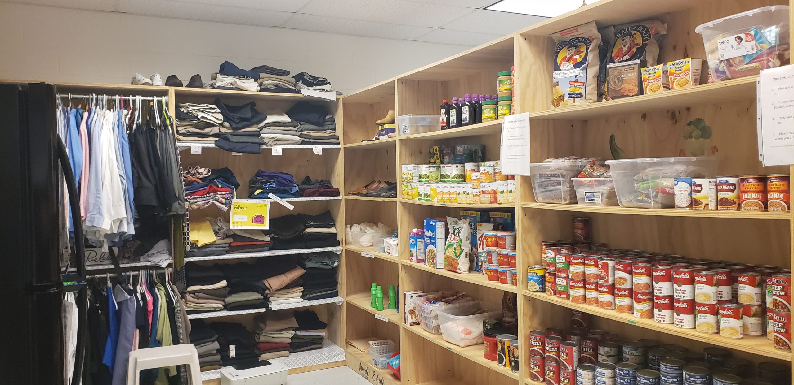 A wide shot of a food pantry stacked with cans of soup and other foods next to a sheft with folded clothes on it