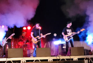 Three guitarists and one drummer on a stage surrounded by smoke during Charlottesville's battle of the bands