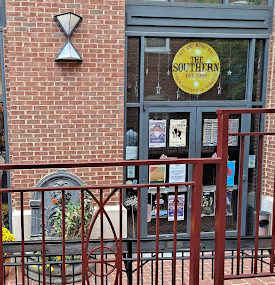The front entrance of the Southern Cafe, a brick building with two double glass doors with a yellow logo on a glass window above the entrance