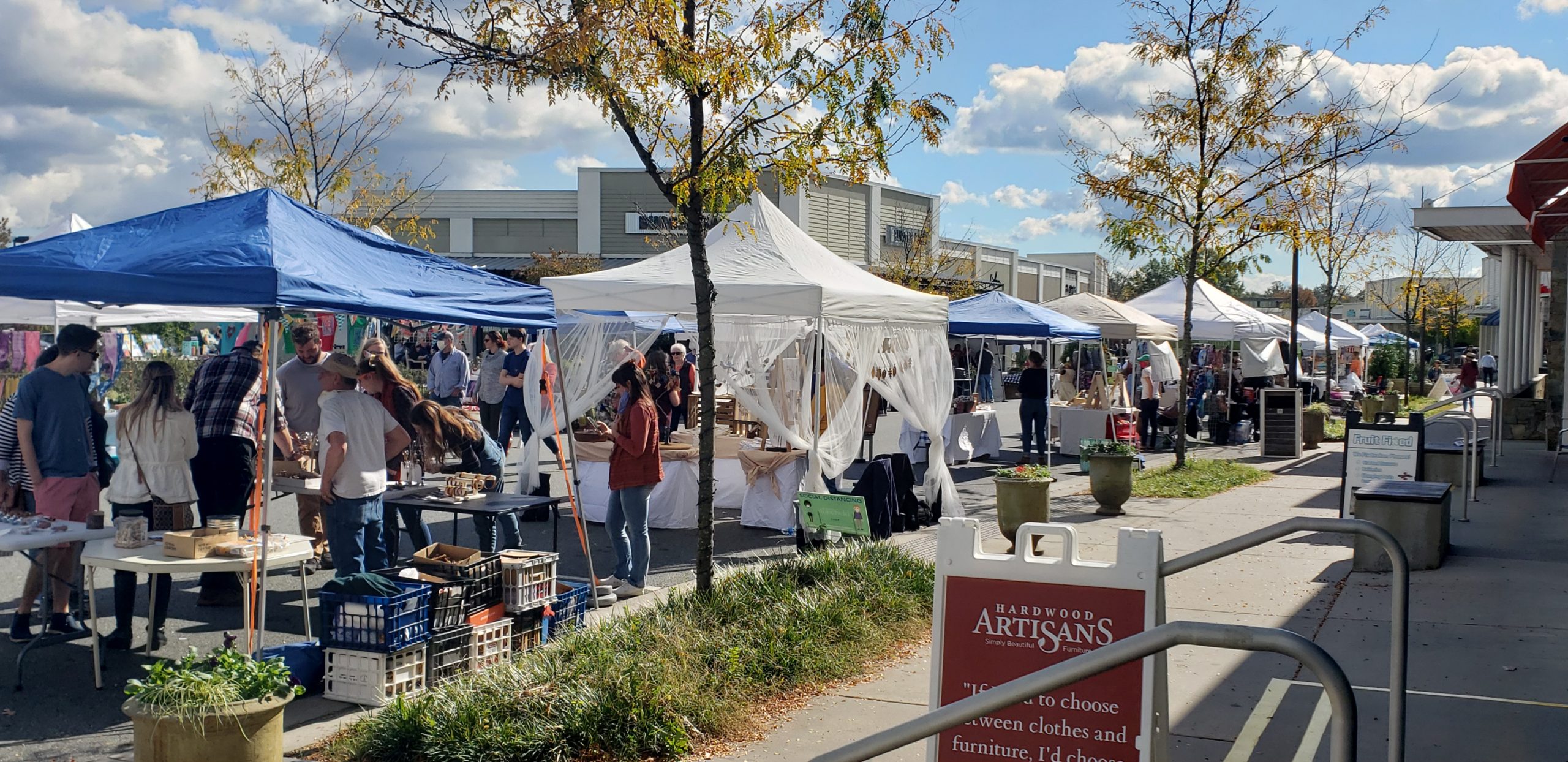 A line of various outdoor tents sell their wares to crowds of customers at the Craft Cville Pop-up Market