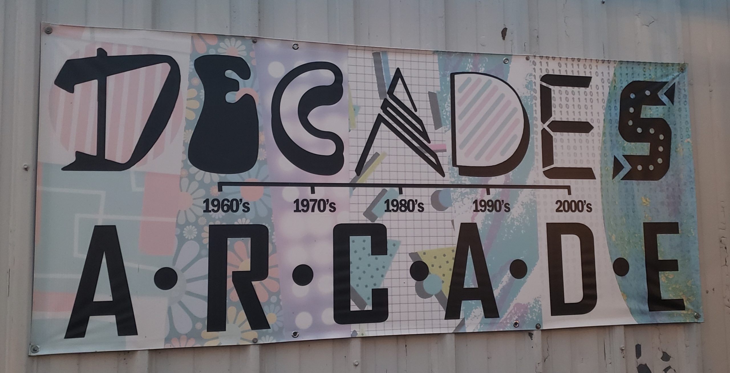 A vintage sign with Decade Arcade's name in varrying black letters