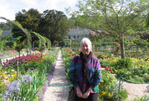 Kristine Swanson standing in a colorful garden full of flowers and trees.