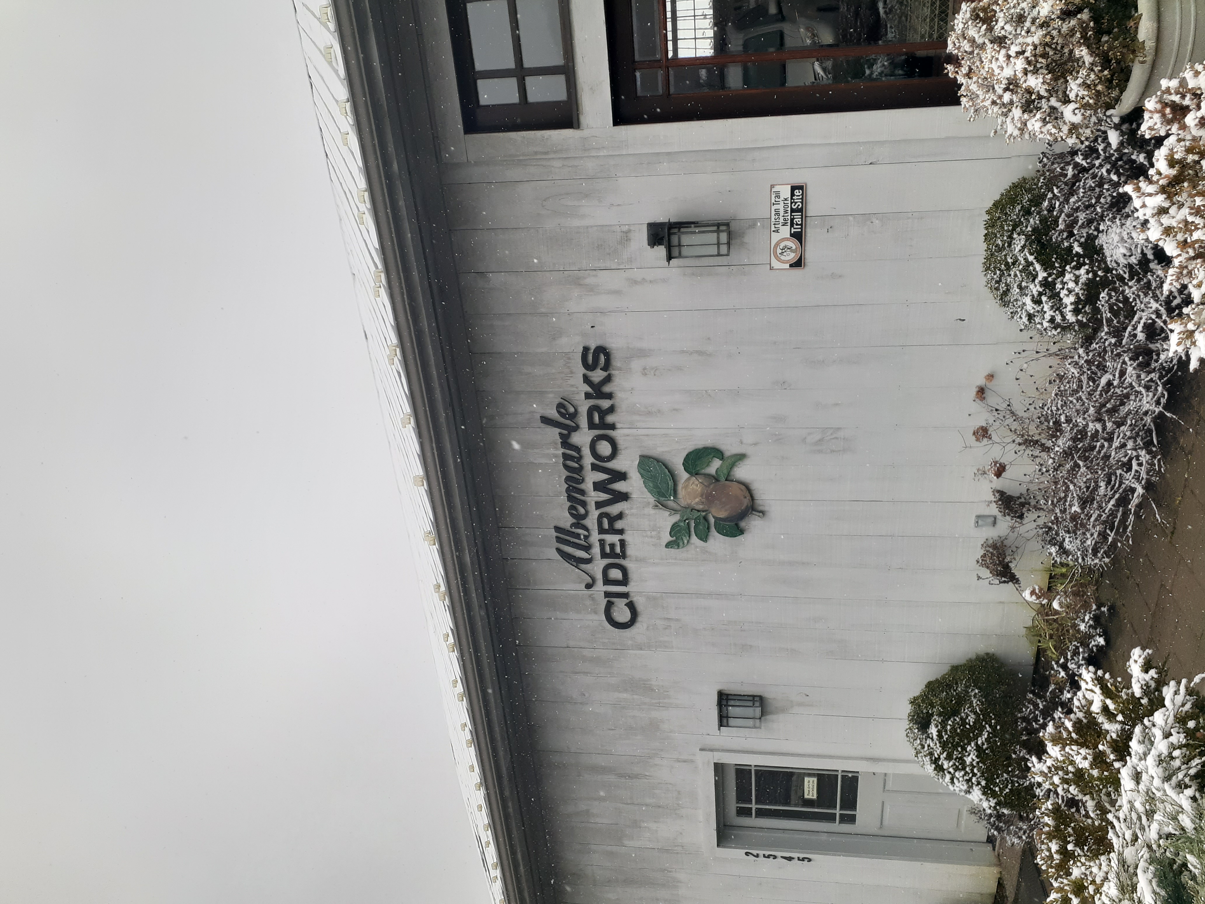 The front of a building with snow peppered around and the Albemarle CiderWorks sign on it.
