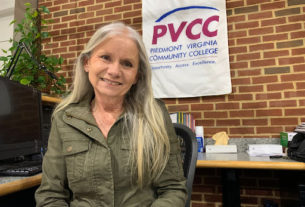 Tomlin sitting at the front desk in a green button down shirt with a PVCC banner behind her.