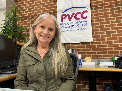 Tomlin sitting at the front desk in a green button down shirt with a PVCC banner behind her.