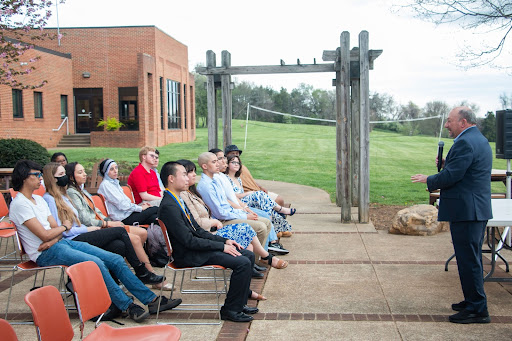 Frank Friedman speaks to a group of students sitting in chairs on the student patio on a cloudy day