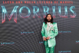Jared Leto poses at the Madrid promotional showing of Morbius. Leto is wearing a lime green suit in front of a Morbius promotional backdrop in Spanish.